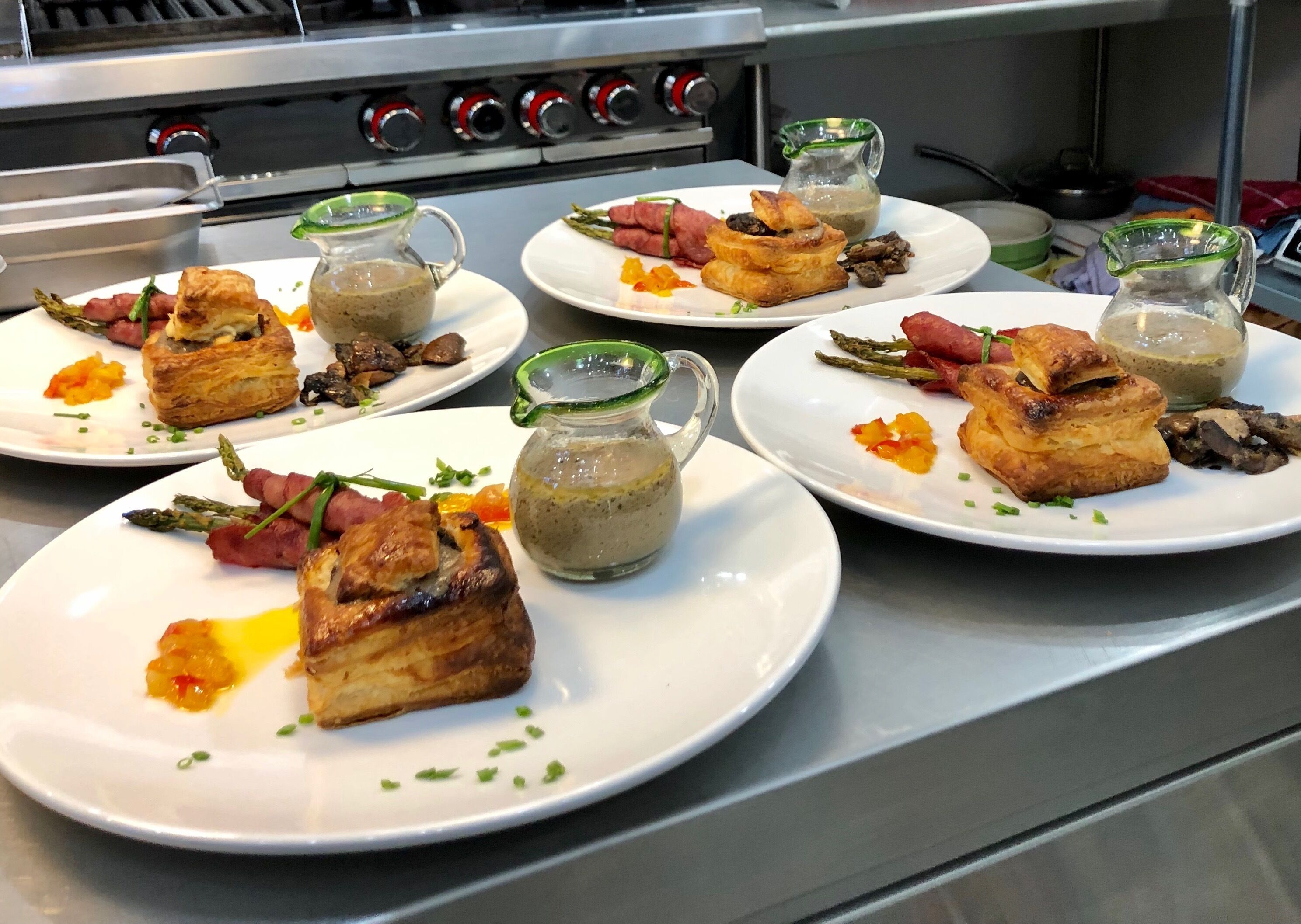 A kitchen with multiple plates of food, including pastries and vegetables, and a stove in the background.