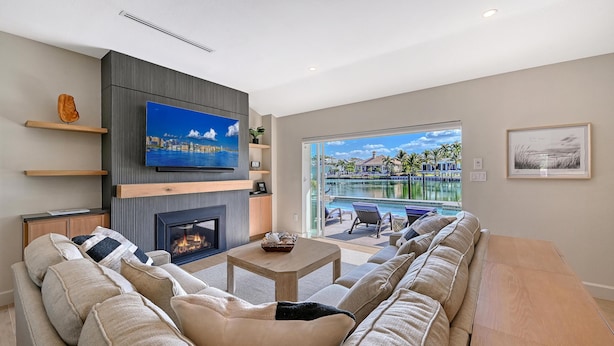 A modern living room with a fireplace, a flat-screen TV, a sofa, and a view of a pool and buildings.