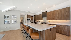 A modern kitchen with a central island, wooden cabinets, and bar stools.