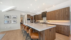 A modern kitchen with a central island, wooden cabinets, and bar stools.