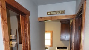 A narrow hallway with wooden flooring, a laundry area with a washing machine, and a sign indicating 'HIKING TRAILS'. - 3/4 Mile from Wilderness Rider Buffalo Ranch,near Buffalo River w/RV Elec Hookup (Kingston)