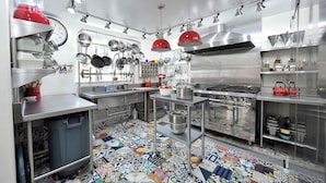 Une cuisine moderne, dotée d’appareils électroménagers en acier inoxydable, d’une variété de casseroles et de poêles suspendues au mur, et d’un sol carrelé aux couleurs vives.