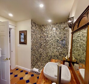 Un baño con pared de mosaicos, un lavamanos blanco y un mueble de tocador de madera.