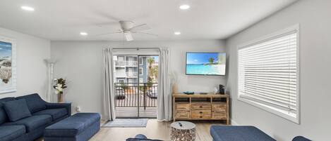 A modern living room with a blue sofa set, a wooden cabinet, and a television on the wall.