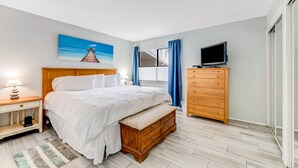 A bedroom with a bed, a wooden dresser, a television, and a painting of a beach scene.