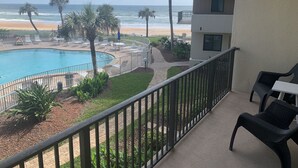 A pool with lounge chairs, a view of the beach, and a building with balconies.