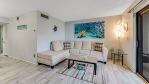 A modern living room with a sectional sofa, a coffee table, and a wall-mounted artwork of a turtle.