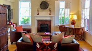 A cozy living room with a fireplace, wooden beams, and a large window.