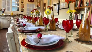 A dining table set with red glassware, white napkins, and plates, with a chandelier and bookshelves in the background.