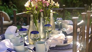 An outdoor dining table set with white and blue tableware, clear glassware, and a floral centerpiece.