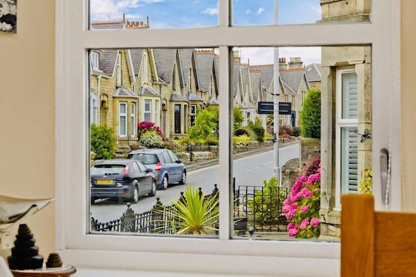 Blick durch ein Fenster auf eine Straße mit traditionellen Häusern, eine Straße und parkende Autos.