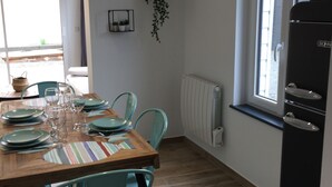 Zona de dinar amb taula de fusta preparada per a quatre, cadires color turquesa i un frigorífic negre.