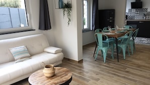 Un saló modern amb un sofà blanc, una taula de centre rodona de fusta, i una zona de menjador amb caires de color turquesa i una taula de fusta.