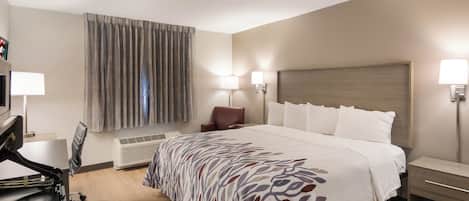 Habitación de hotel con cama, escritorio, silla, televisor y ventana con cortinas.