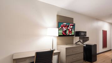 A hotel room with a desk, chair, TV, and a microwave.