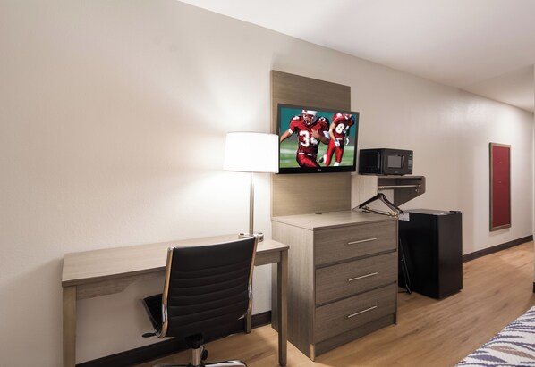 A hotel room with a desk, chair, TV, and a microwave.