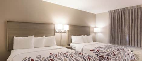 A hotel room with two beds, a headboard, bedside lamps, a window with curtains, and an air conditioning unit.