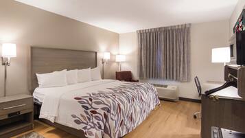A hotel room with a bed, bedside tables, a desk, a chair, a window with curtains, and a wall-mounted TV.