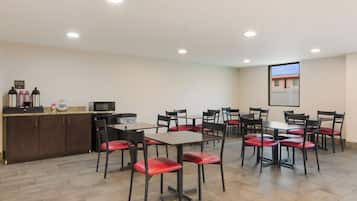 A conference room with tables and chairs, a kitchenette, and a projection screen on the wall.