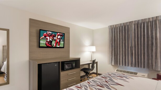 A hotel room with a bed, a desk with a computer, a television mounted on the wall, and a window with curtains. - Red Roof Inn Chester (Chester)