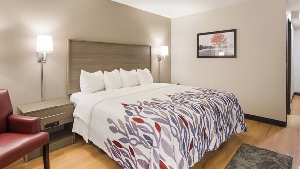 A hotel room with a bed, bedside tables, a chair, and a framed picture on the wall. - Red Roof Inn Chester (Chester)