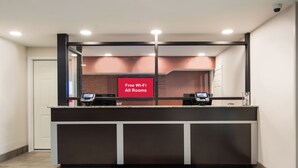 A reception desk with a digital display, a 'Free Wi-Fi All Rooms' sign, and a 'Red Roof Inn' mat. - Red Roof Inn Chester (Chester)