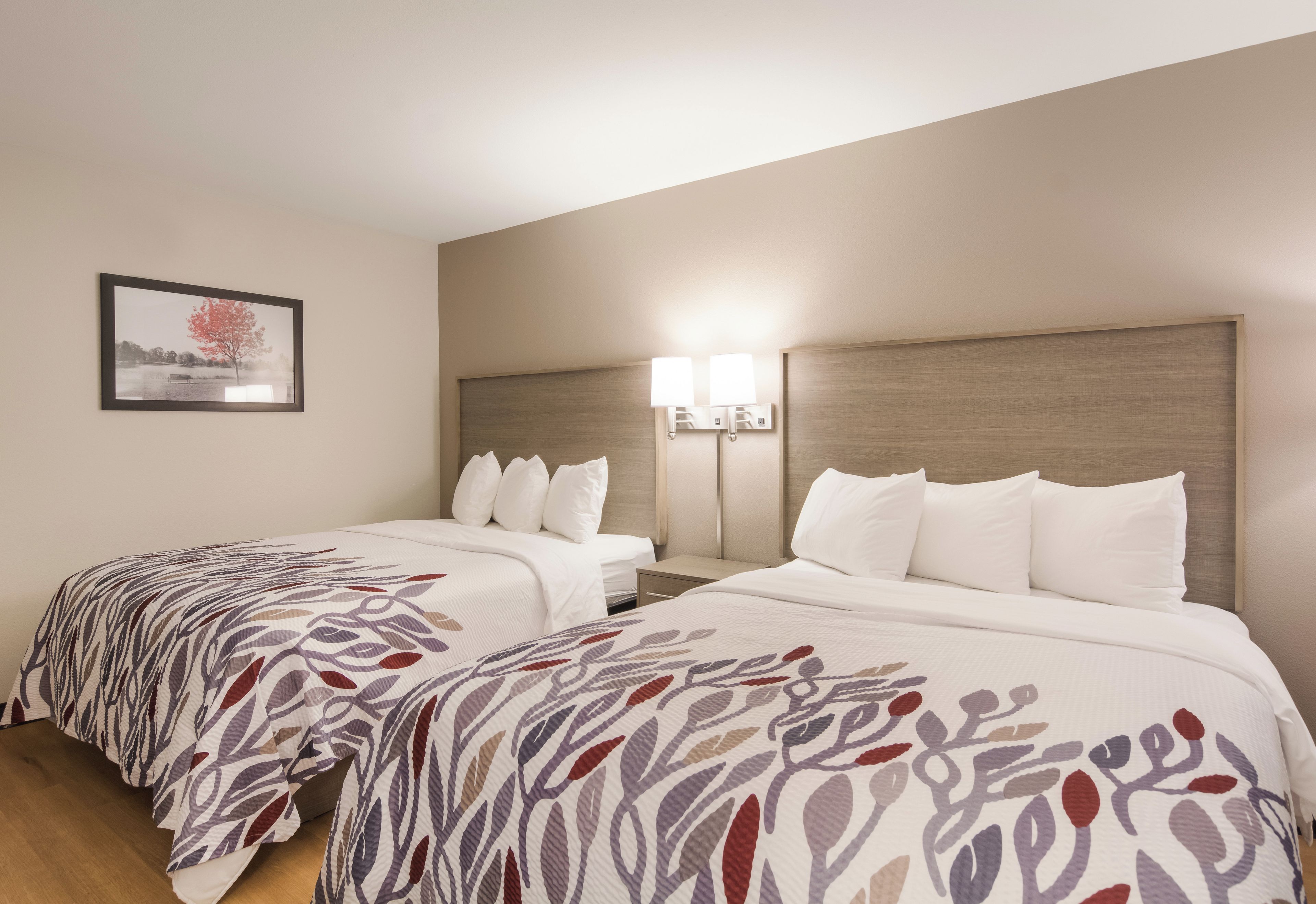 Habitación de hotel con dos camas, una mesita de noche, una lámpara y un cuadro en la pared.