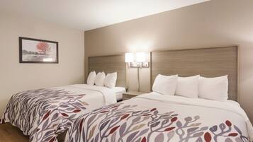 Habitación de hotel con dos camas, una mesita de noche, una lámpara y un cuadro en la pared.