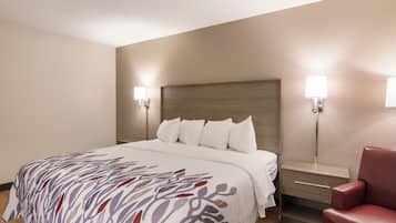 Habitación de hotel con cama, mesitas de noche, una silla y lámparas de pared.