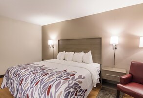 Habitación de hotel con cama, mesitas de noche, una silla y lámparas de pared.