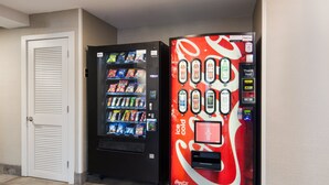 Dans un couloir, on trouve deux distributeurs automatiques, l’un arborant le logo Coca-Cola et l’autre celui de Pepsi.