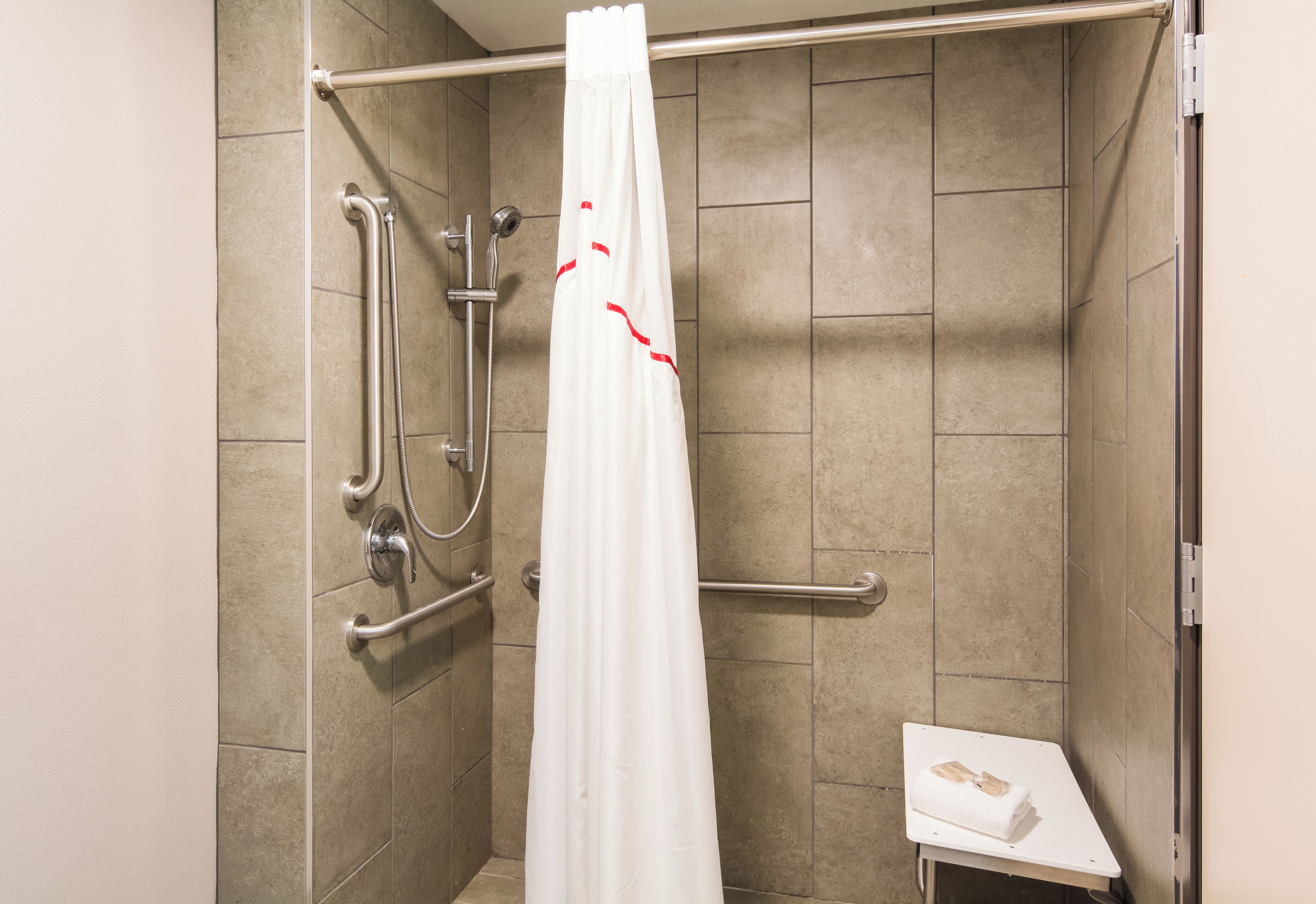 A shower area with a white curtain, grab bars, and a small table with a towel.