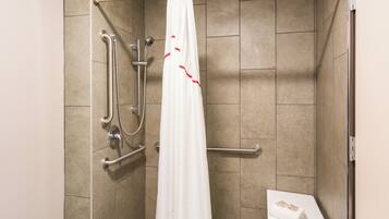 A shower area with a white curtain, grab bars, and a small table with a towel.