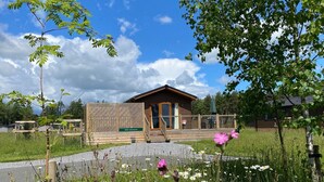 A small wooden cabin with a porch, surrounded by a grassy field and blooming flowers. - Hollicarrs - Newlands (York)