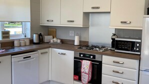 A modern kitchen with white cabinetry, a dishwasher, a stove, and a microwave. - Hollicarrs - Newlands (York)