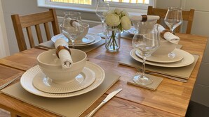 A dining table set with white bowls, plates, and cutlery, with a vase of white flowers and a window view. - Hollicarrs - Newlands (York)
