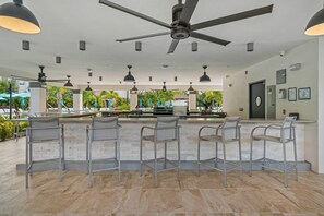 A bar area with a ceiling fan, multiple hanging lights, and a view of the outdoor pool area.