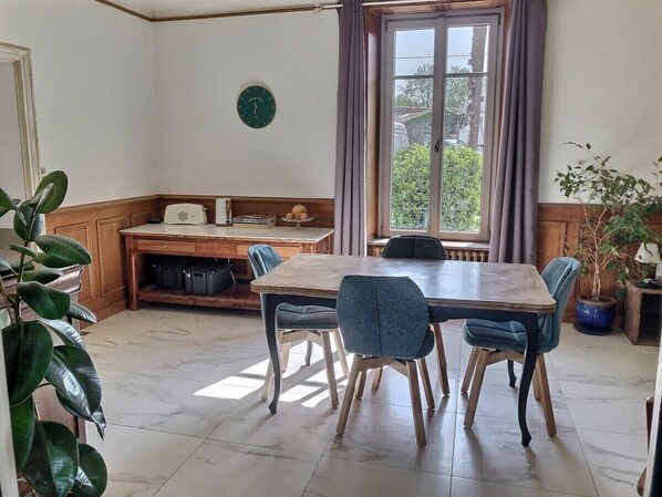 Un coin repas avec une table en bois et quatre chaises, un coin cuisine avec un évier et des placards, et une fenêtre avec des rideaux.