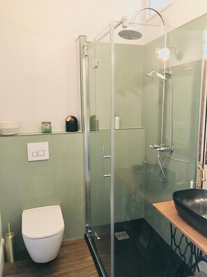 Un bagno moderno con cabina doccia in vetro, un water bianco e un mobile bagno in legno con lavandino nero.