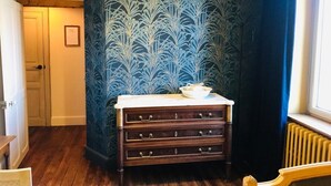 A room with a wooden dresser, a patterned wallpaper, a radiator, and a door.