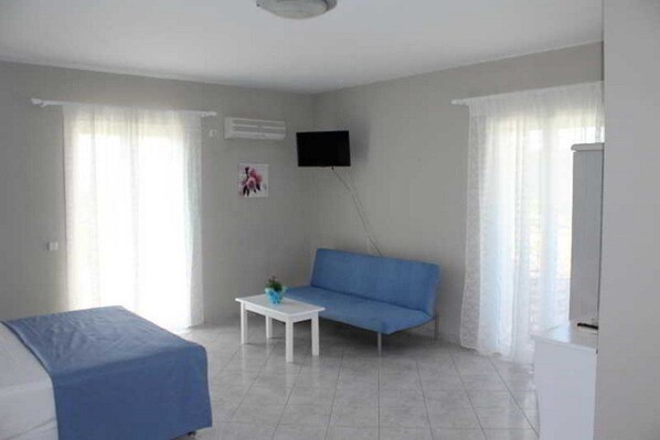 A small, modern room with a blue sofa, a white table, and a TV mounted on the wall.