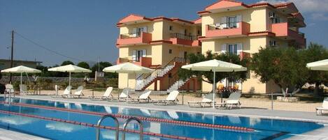 A hotel with a swimming pool, sun loungers, and umbrellas.