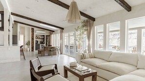 A spacious living room with a large sofa, a coffee table, and a dining area with a kitchen in the background. - Wind Hill in Pioneertown & Joshua Tree (Yucca Valley)