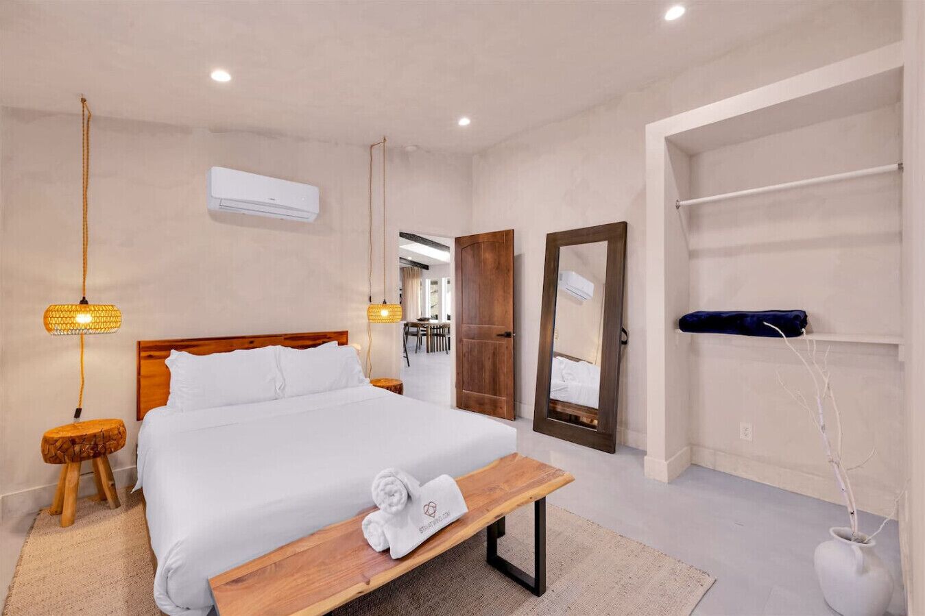 A modern hotel room with a wooden bed, bedside lamp, and a bench with a towel.