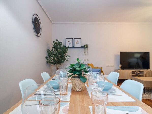 Un espace repas avec une longue table en bois, de la vaisselle transparente et des chaises bleu clair.