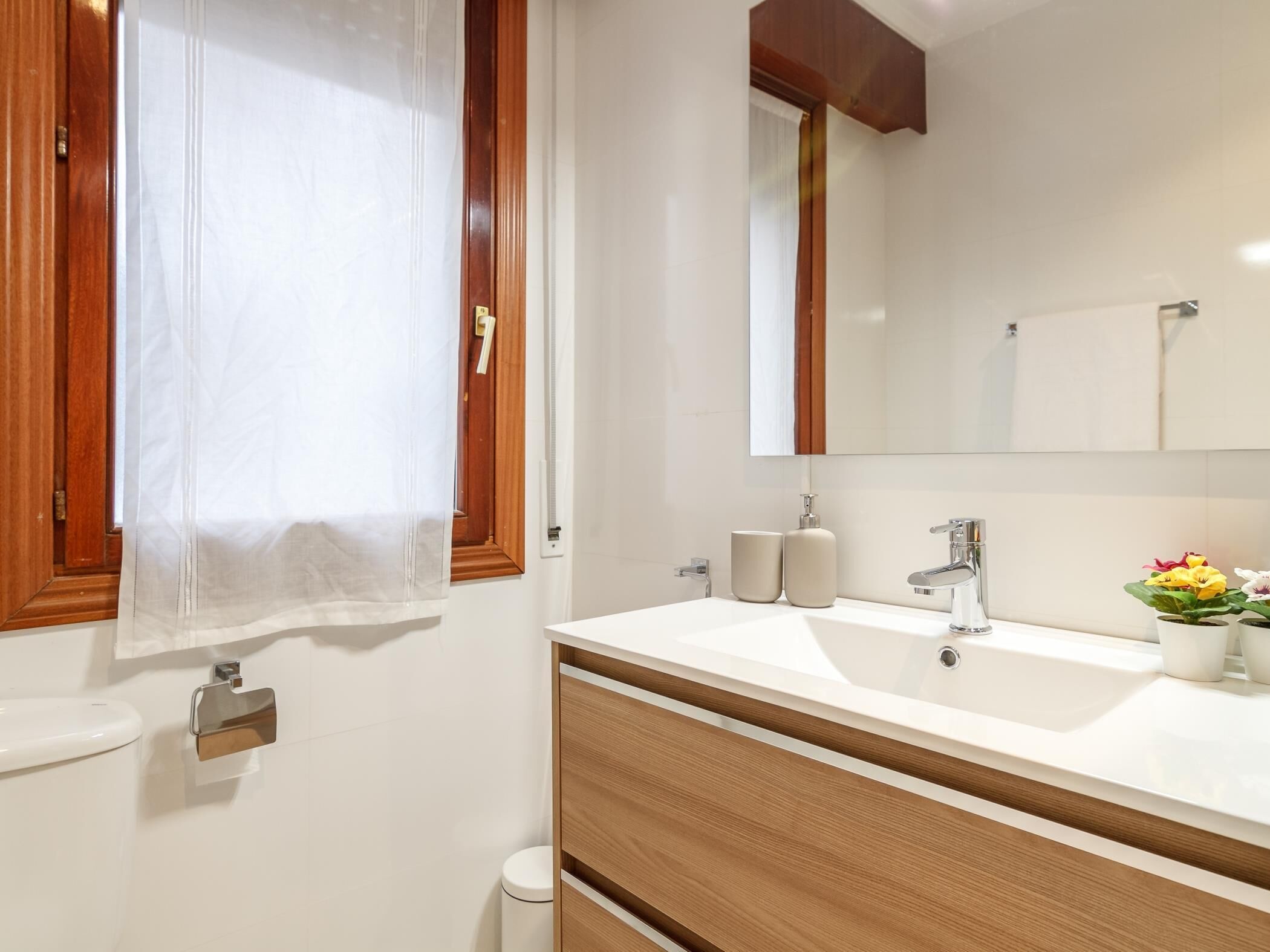 Un baño con tocador de madera, espejo, lavamanos e inodoro.