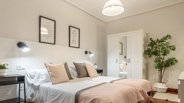 A neatly arranged bedroom with a bed, bedside tables, a wardrobe, and a potted plant. - Amplio y recién reformado en Indautxu (Bilbao)