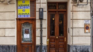 A building with a wooden door and a sign advertising a property for sale. - Amplio y recién reformado en Indautxu (Bilbao)
