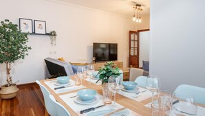 A dining area with a long wooden table set for four, surrounded by light blue chairs. There is a television on the wall and a potted plant to the left. - Amplio y recién reformado en Indautxu (Bilbao)