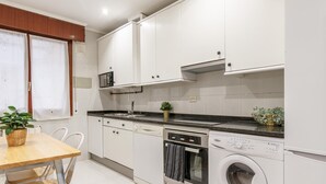 A modern kitchen with white cabinets, a black countertop, a dishwasher, and a built-in washing machine. - Amplio y recién reformado en Indautxu (Bilbao)